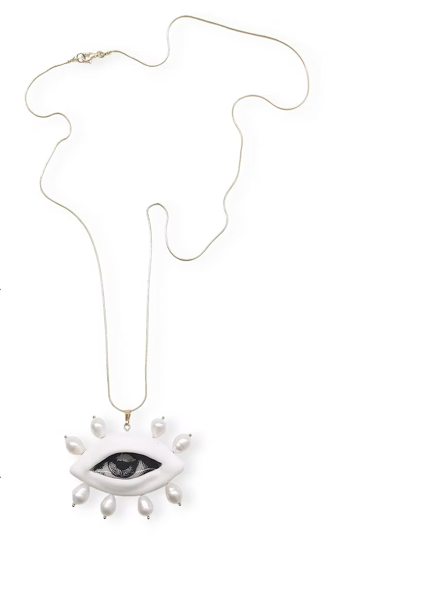 A white eye-shaped pendant necklace with faux pearls arranged around the eye, suspended from a delicate gold chain on a plain white background.