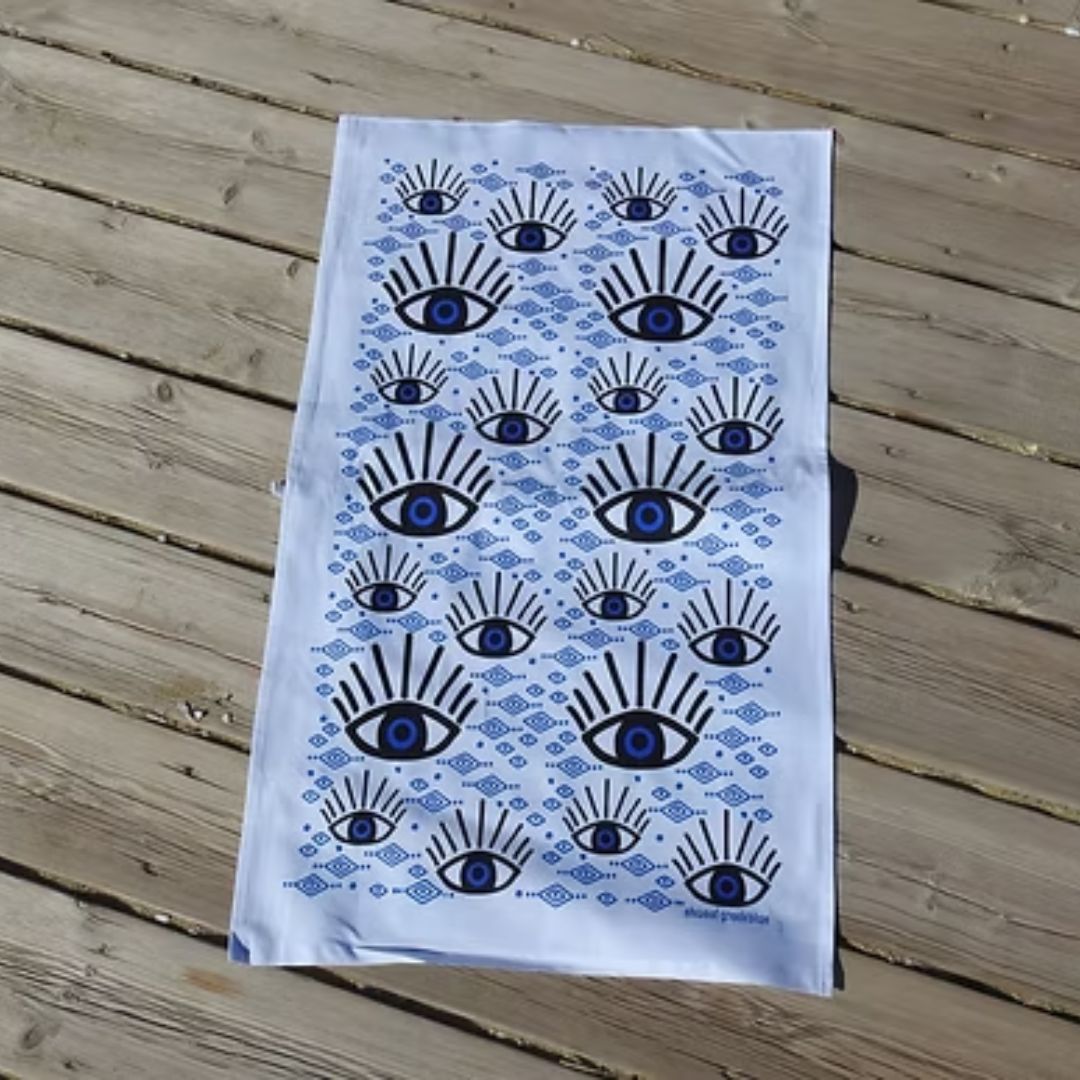 Blue Eye Cotton Tea Towel – screen-printed Greek evil eye design in blue and black on white cotton, styled flat view | Thalassea