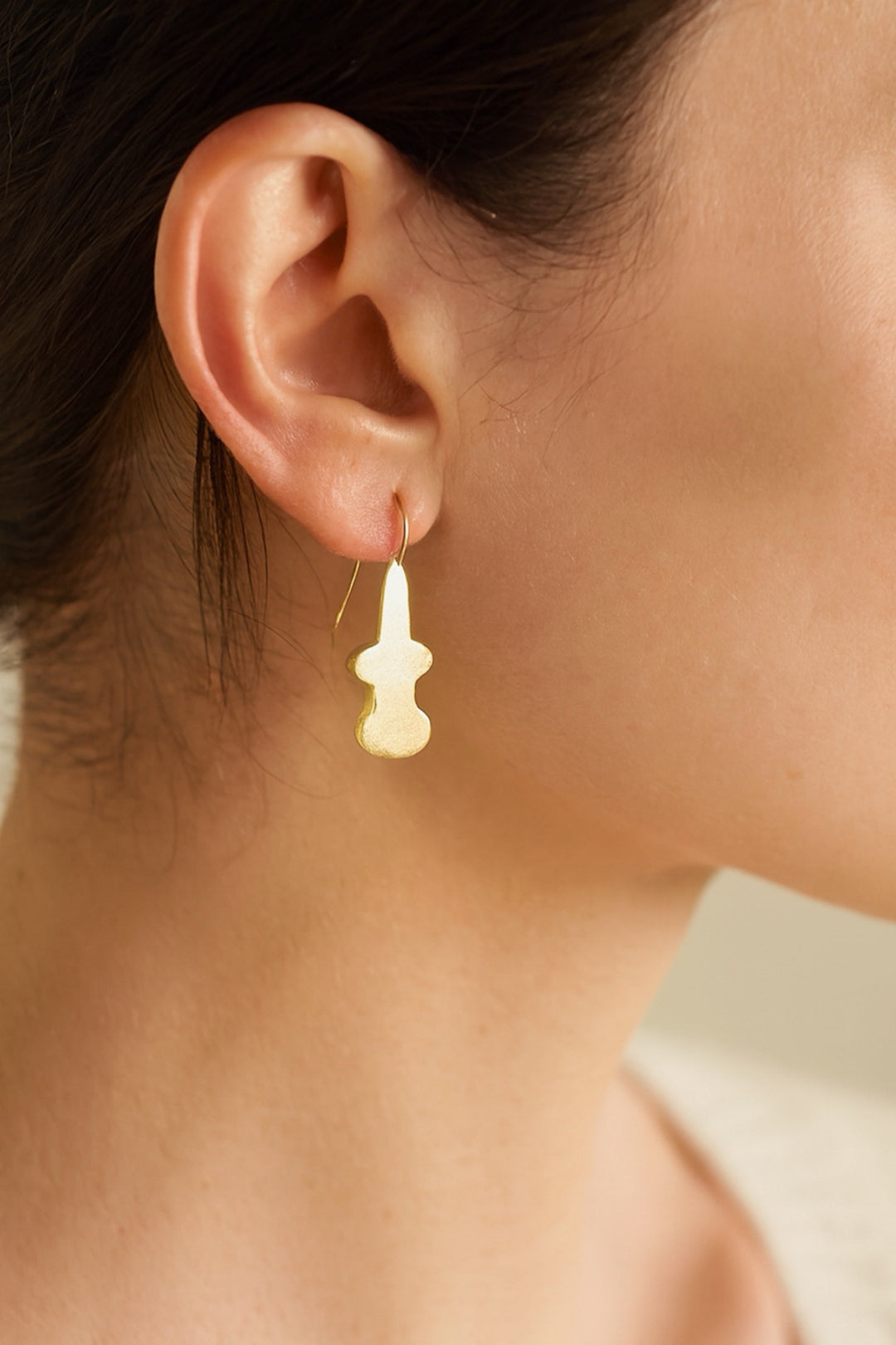 Close-up of an ear wearing a gold earring with a white stone.