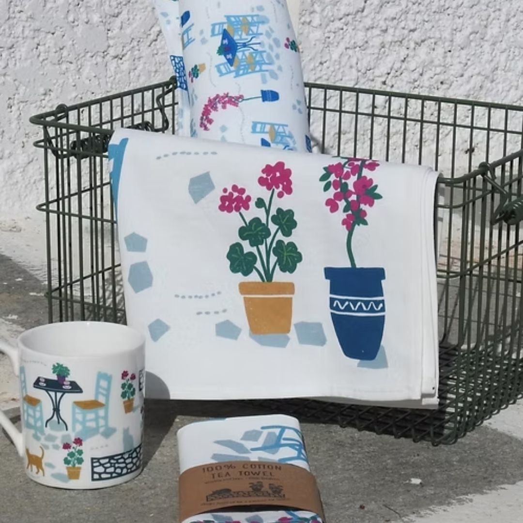 Coffee and Drinks Cotton Tea Towel – geraniums and blue pot print draped over a wire basket with a Greek café mug, styled | Thalassea