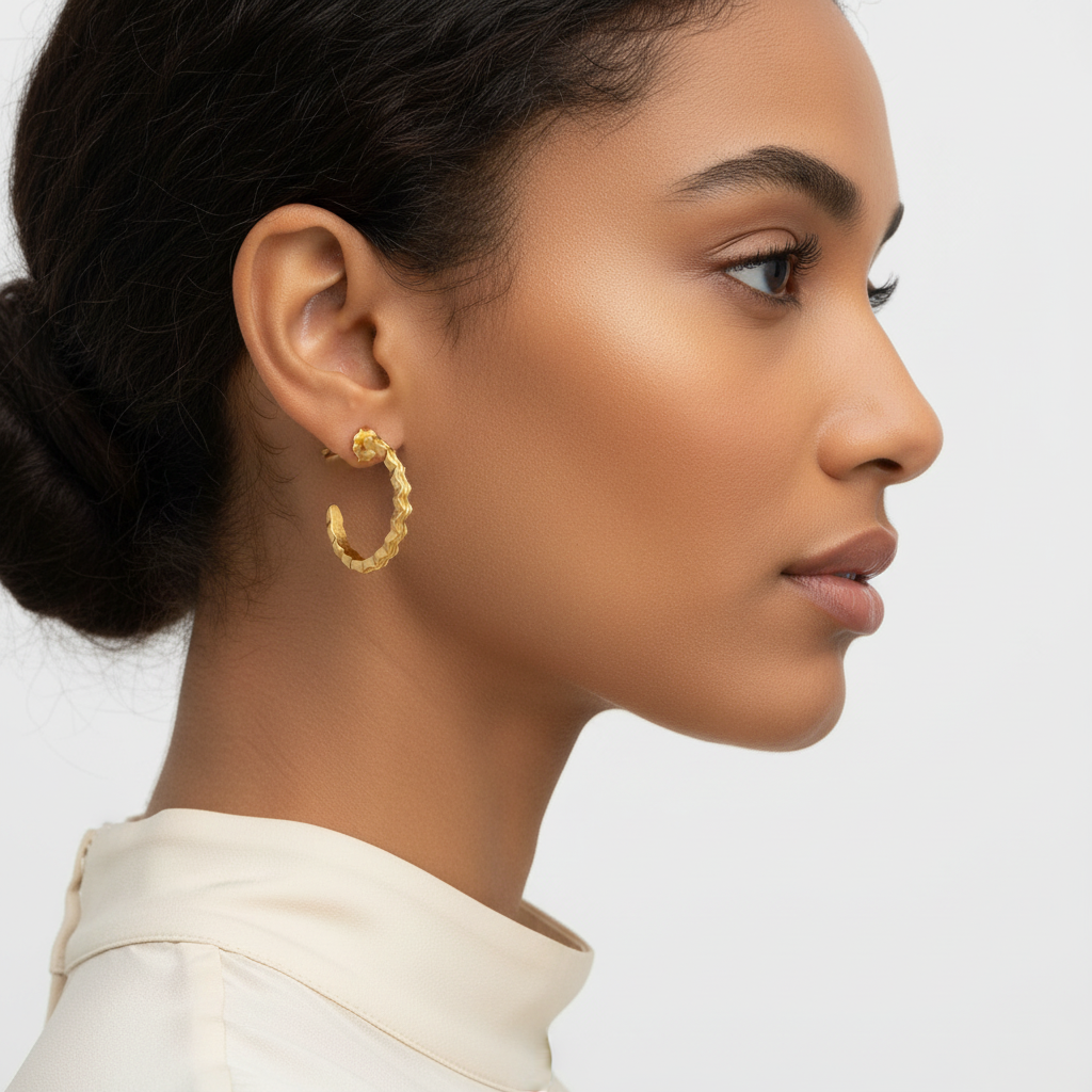 Close-up of a woman wearing gold hoop earrings against a neutral background
