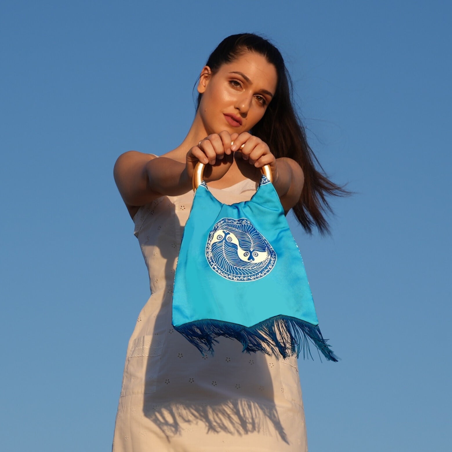 Woman holding a blue handbag with a design against a clear blue sky