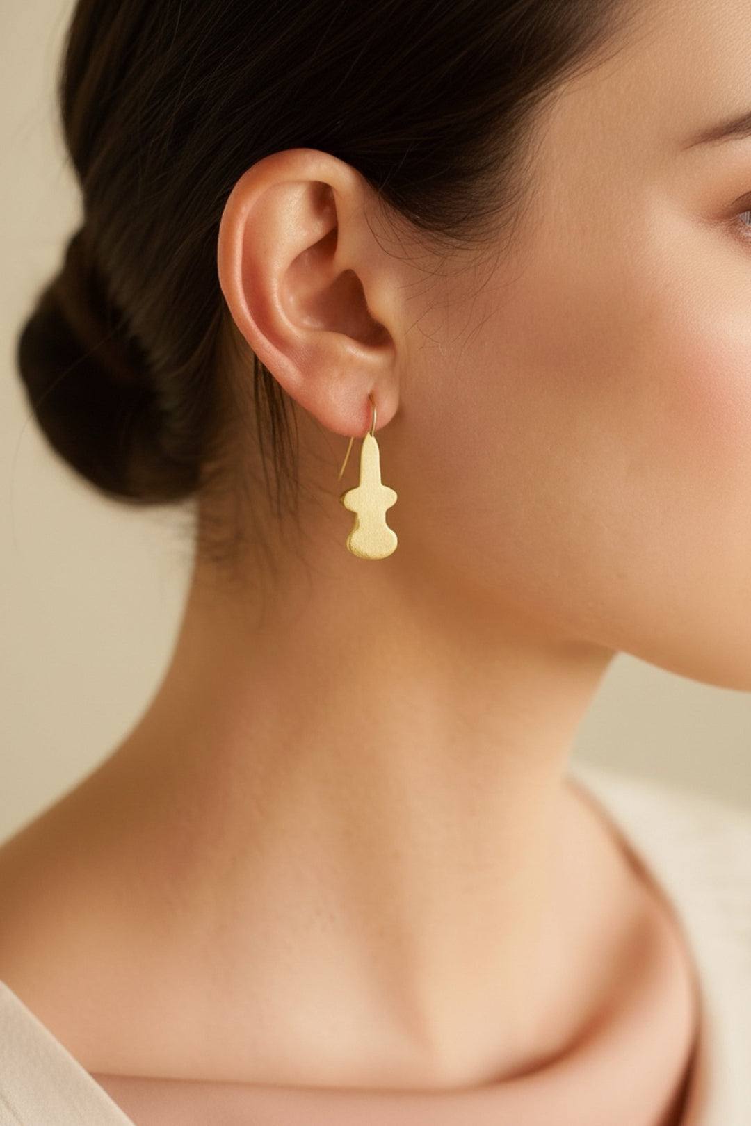 Close-up of a person wearing a gold earring with a neutral background