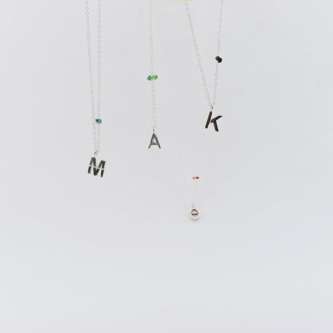 Two necklaces with letter pendants on a white background