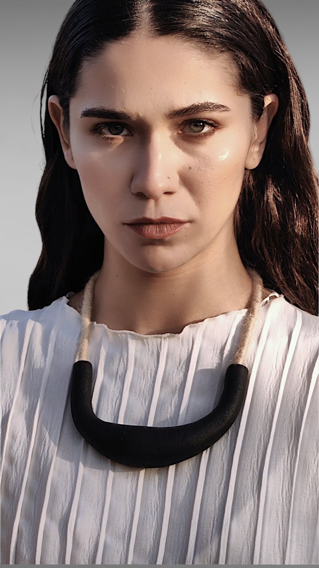 Woman wearing a black necklace against a neutral background