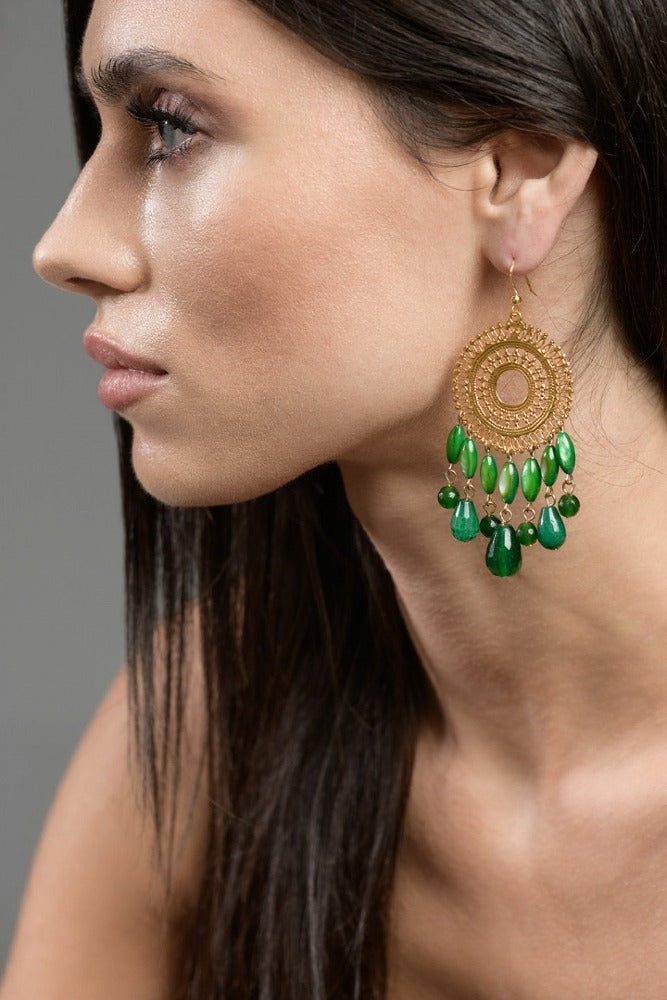 Woman wearing green and gold earrings with a blurred outdoor background