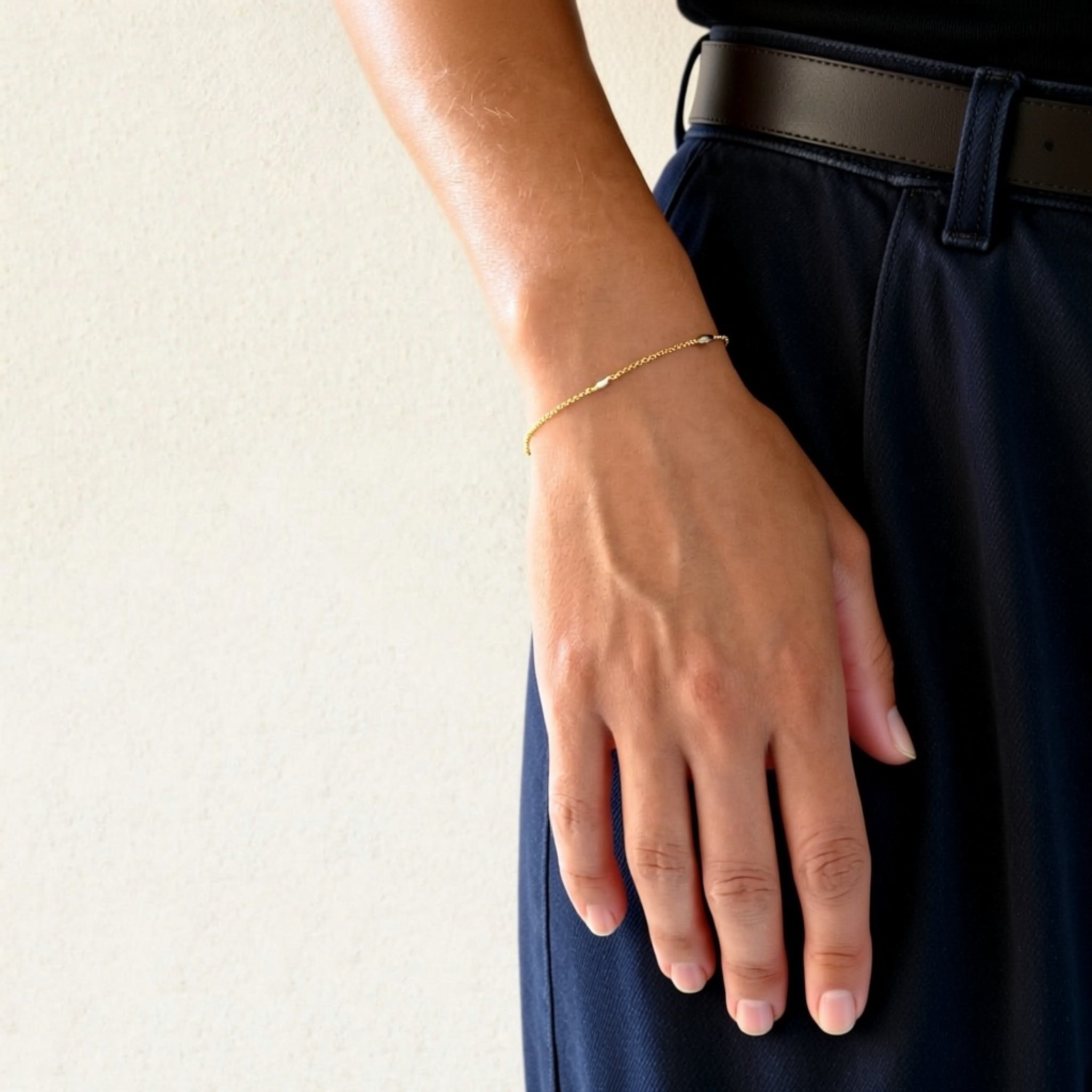 Hand wearing a gold bracelet on a plain background