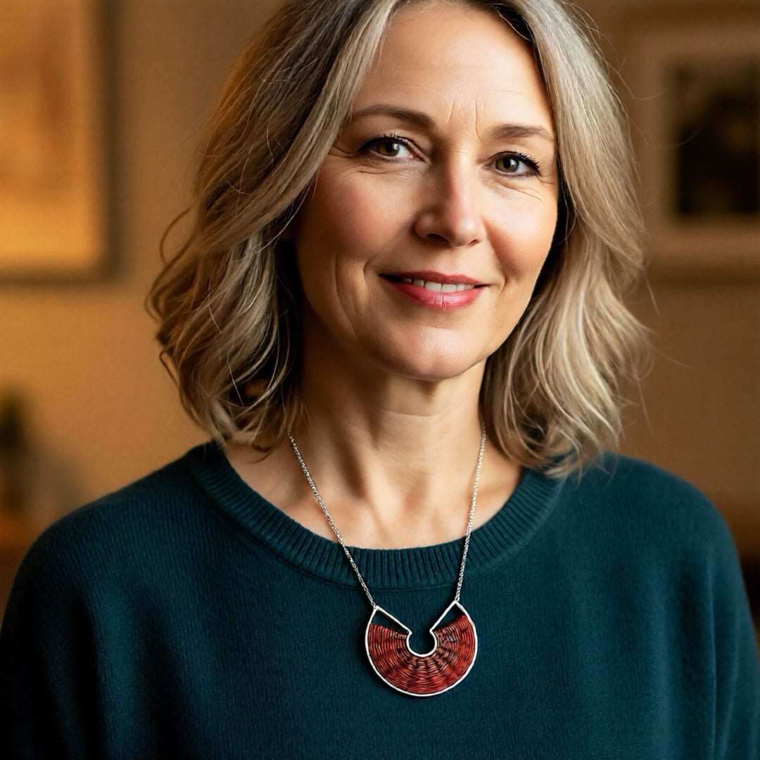 Woman wearing a green sweater and a necklace with a red pendant indoors.