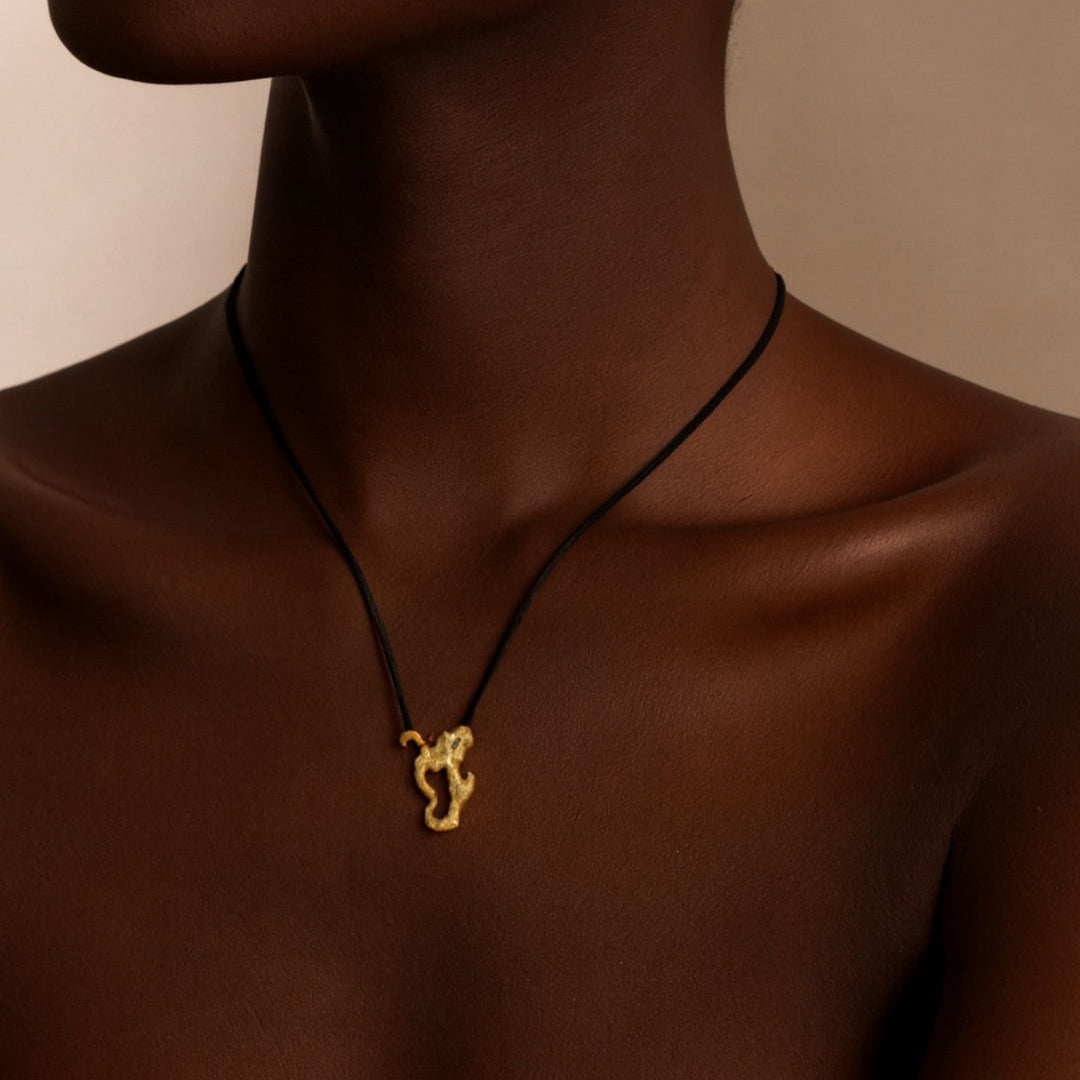 Close-up of a person wearing a gold necklace with a pendant on a neutral background