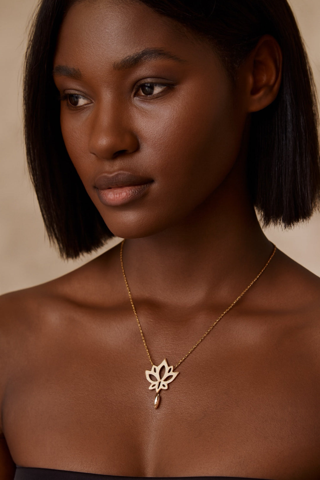 Woman wearing a gold necklace with a lotus flower pendant against a neutral background