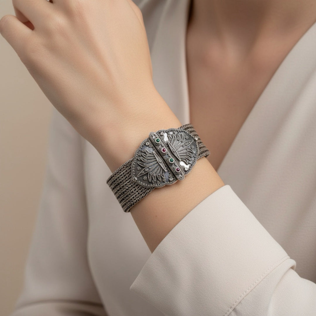 Silver bracelet with gemstones on a wrist, against a neutral background