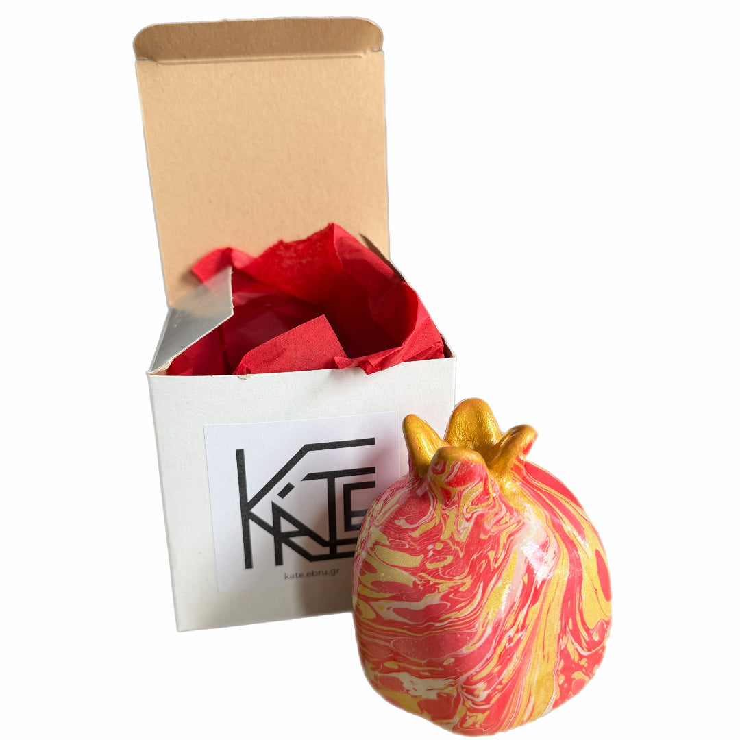 Decorative pomegranate with marbled design next to a branded box on a white background