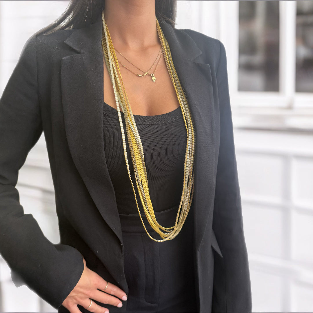 Person wearing a black blazer and multiple gold necklaces with a blurred background
