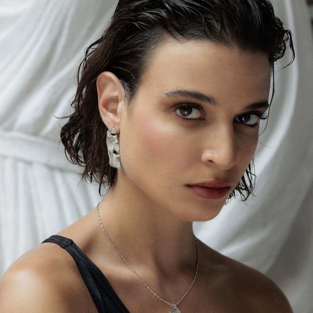 Woman wearing earrings and a necklace against a white curtain background