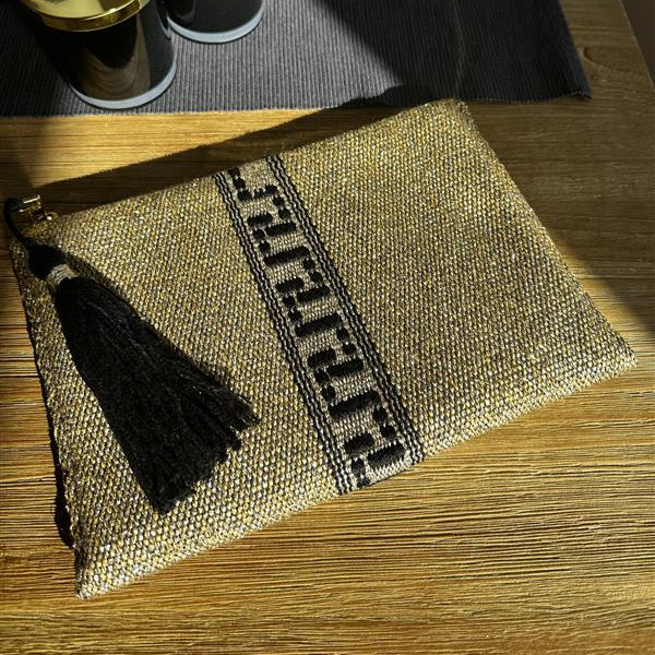 Jute bag with tassels on a wooden surface with black and gold cylindrical objects in the background.