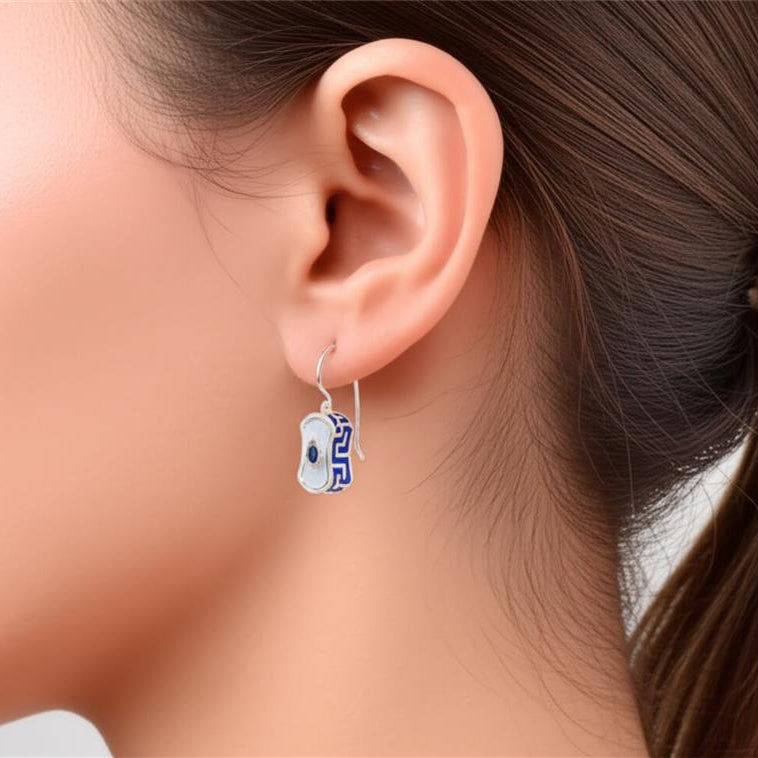 Close-up of an ear wearing a small blue and white earring with a blurred background
