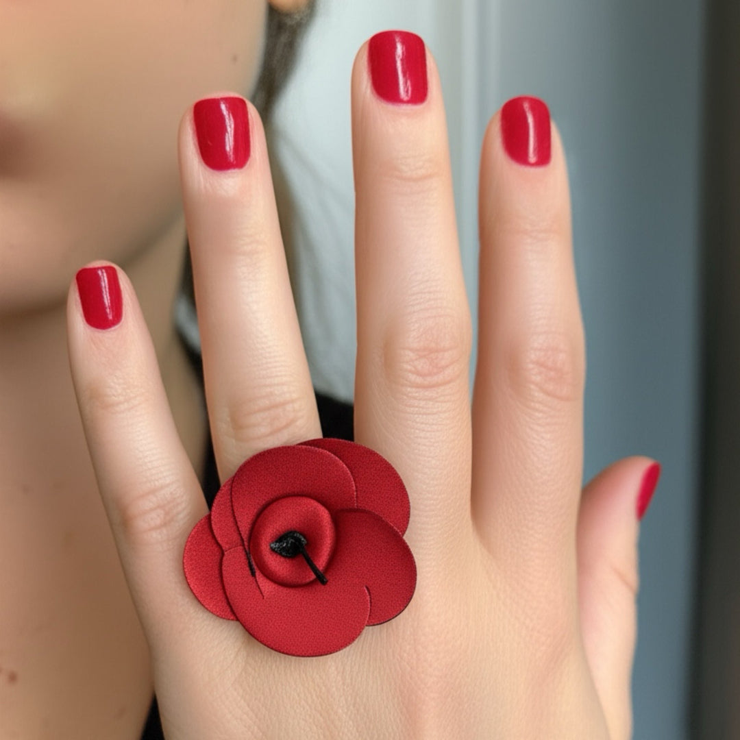Red flower ring on a hand with red nail polish against a neutral background