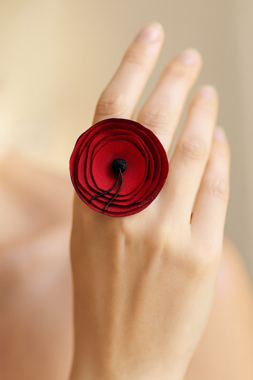 Red flower-shaped ring on a person's finger with a blurred background