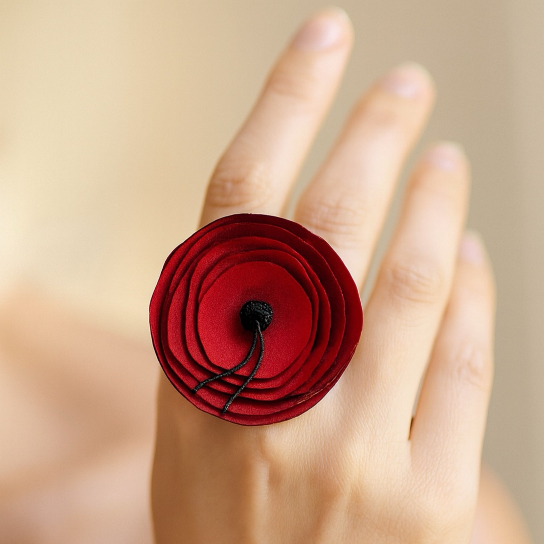 Red flower-shaped ring on a person's finger with a blurred background