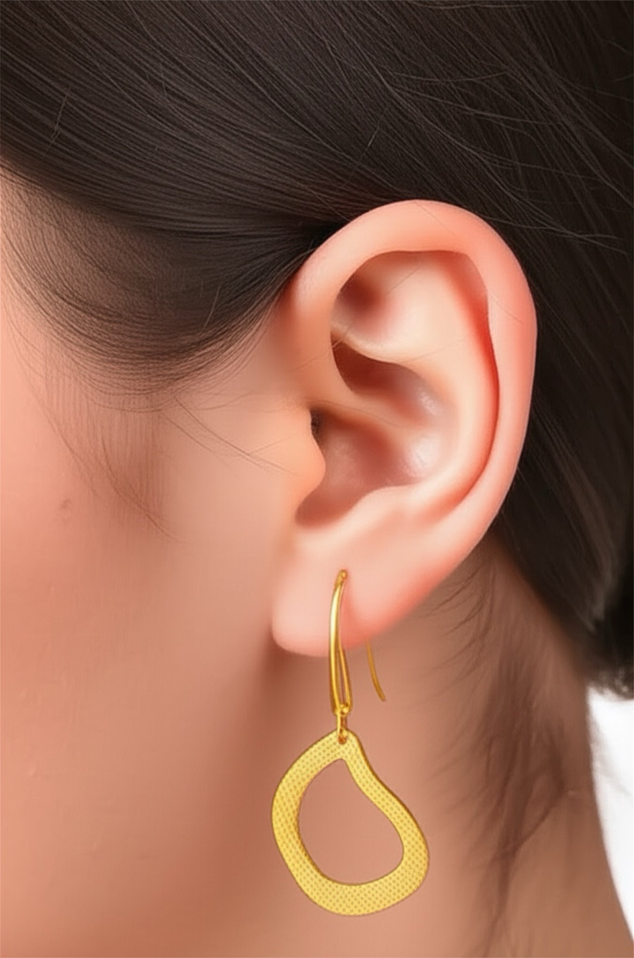 Gold hoop earring worn by a person with dark hair.