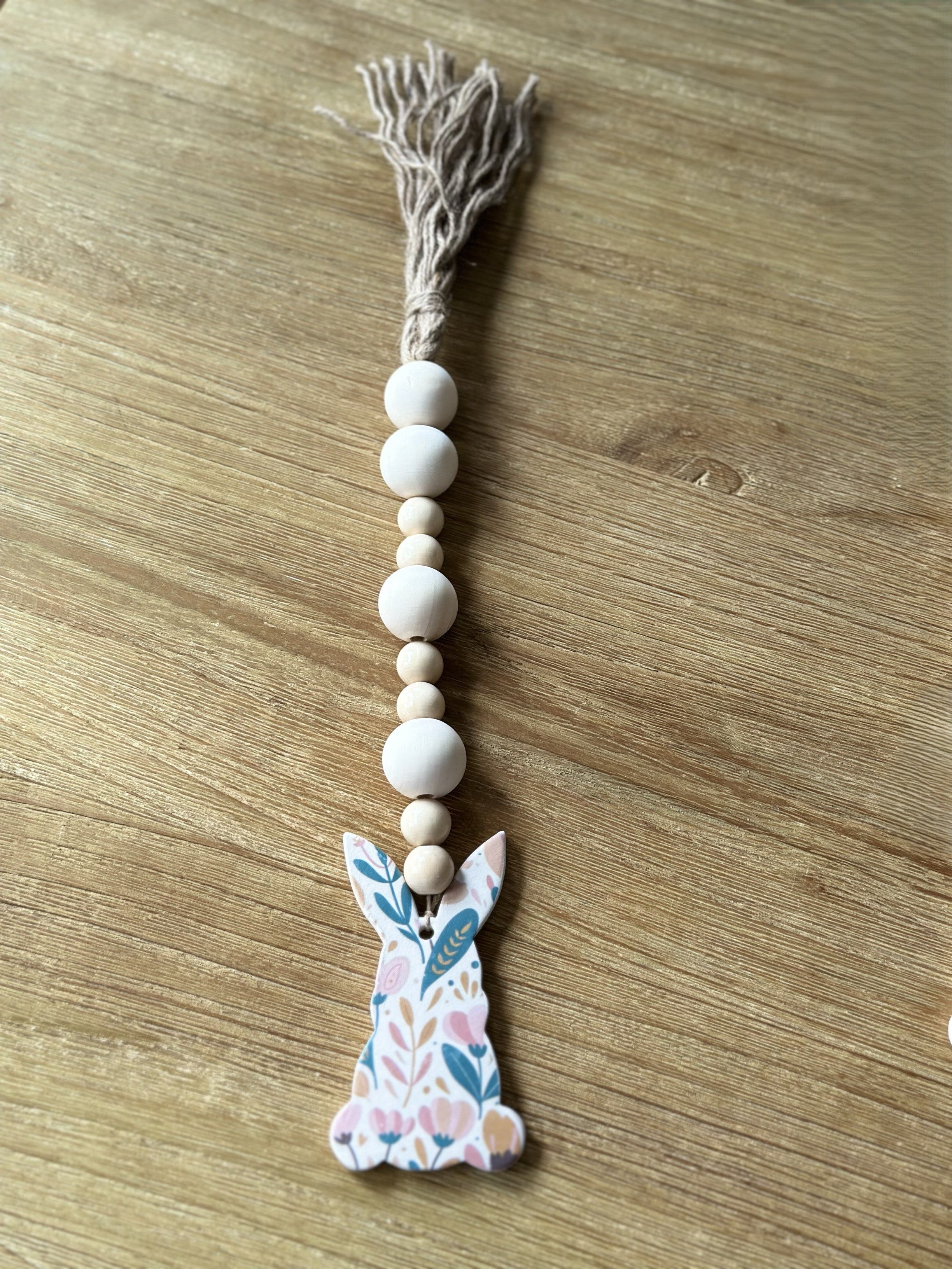 A ceramic Easter ornament in the shape of a bunny, with pastel colors and wooden beads, attached to a tassel.