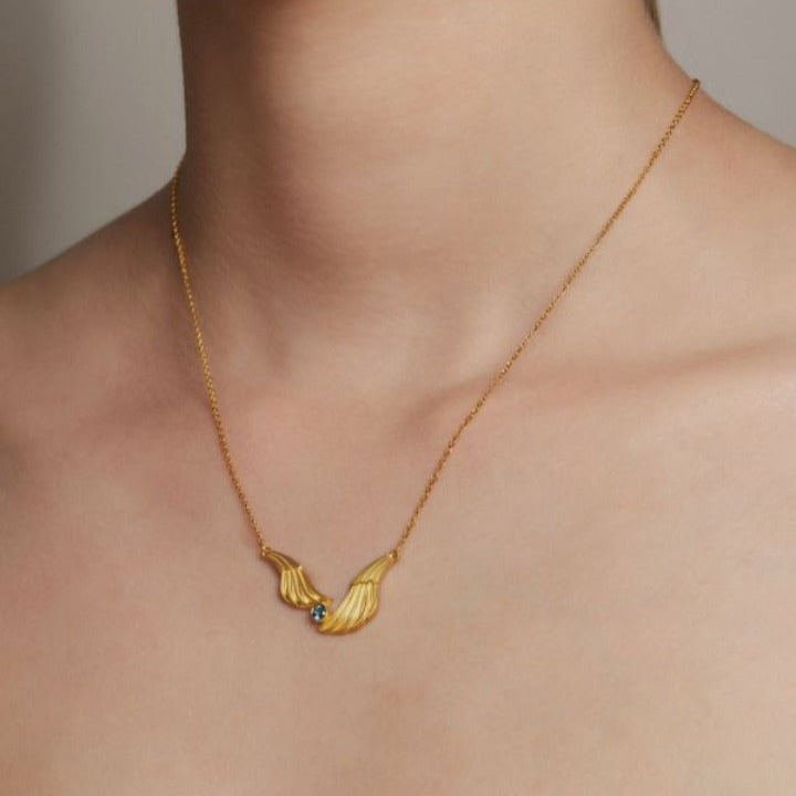 Gold necklace with a leaf-shaped pendant on a neutral background
