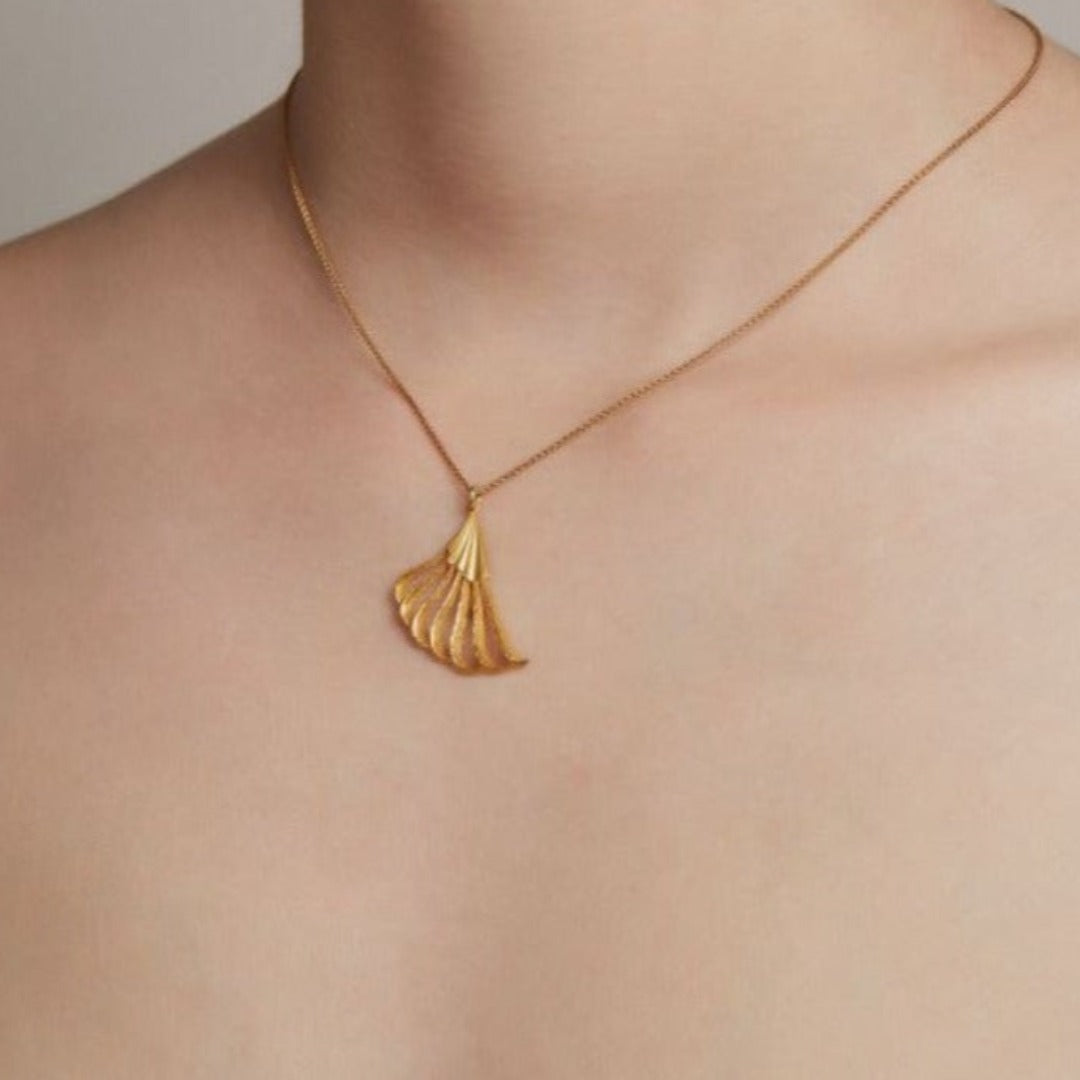 Gold necklace with a fan-shaped pendant on a white background