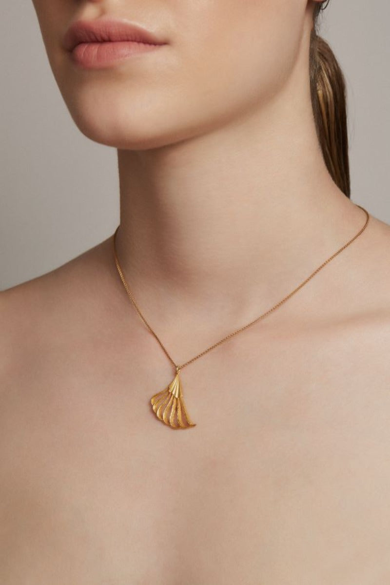 Woman wearing a gold necklace against a beige background