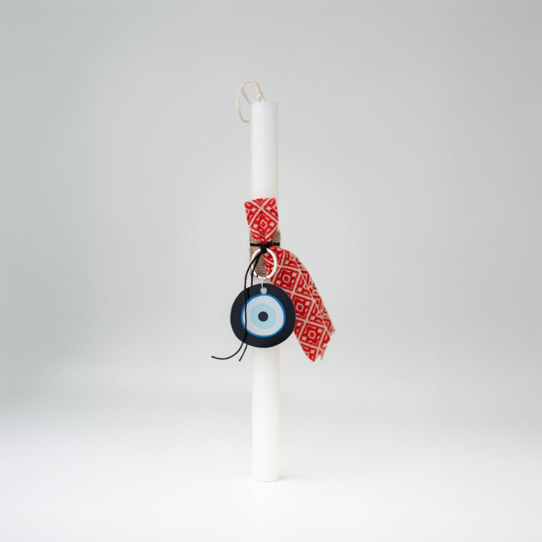 White candle with a red decorative band and an evil eye charm on a white background