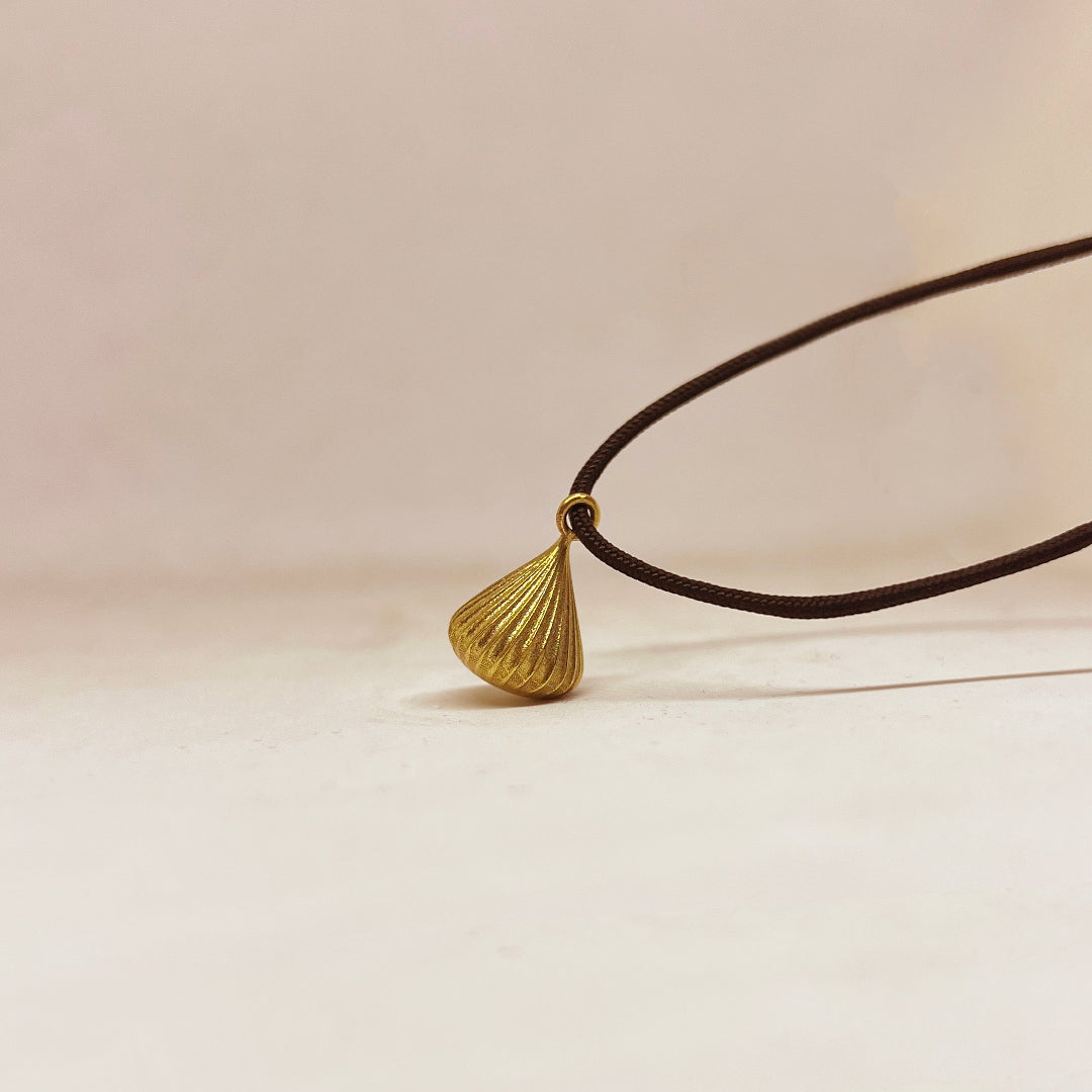Gold pendant on a black cord against a beige background