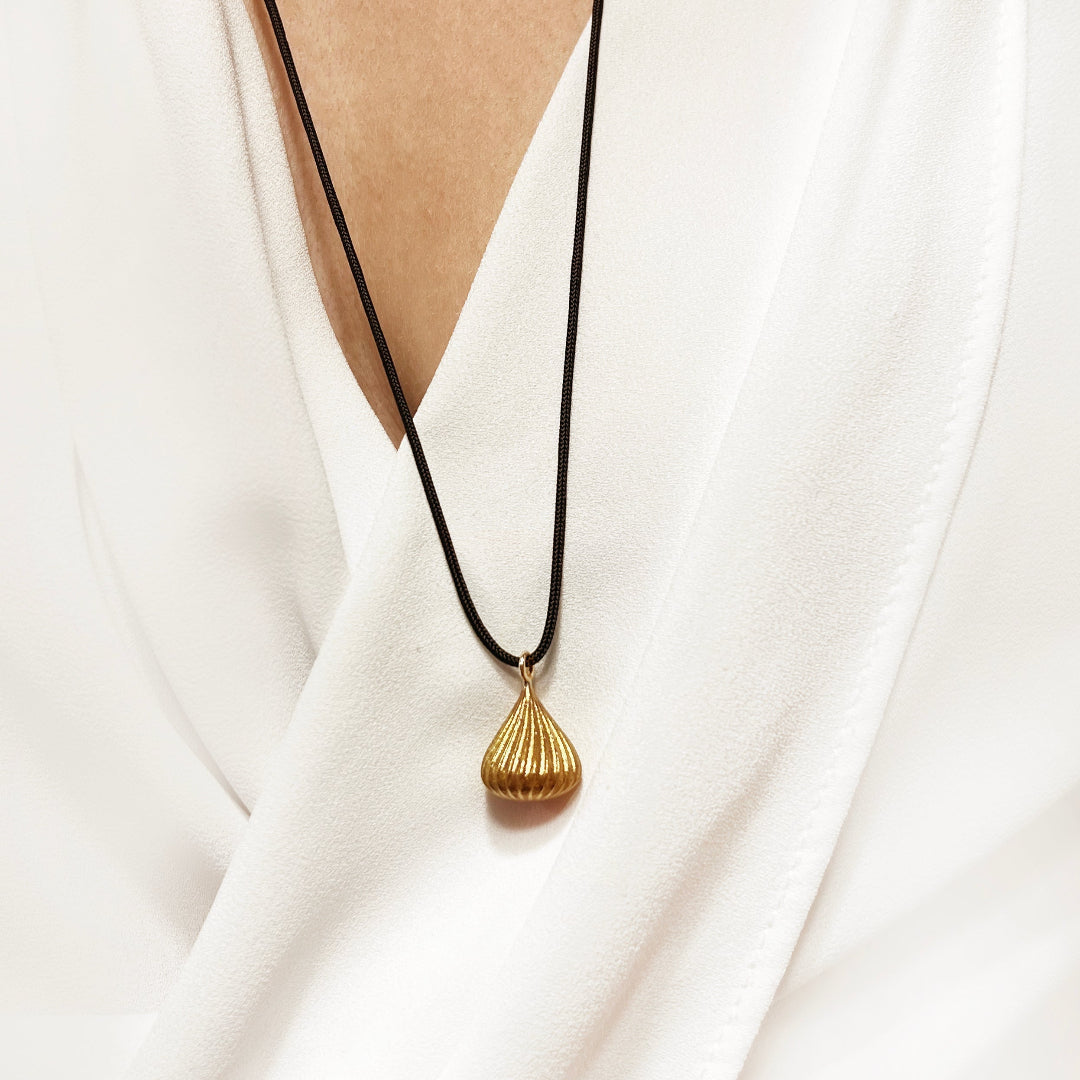 Gold pendant necklace on a black cord against a white fabric background