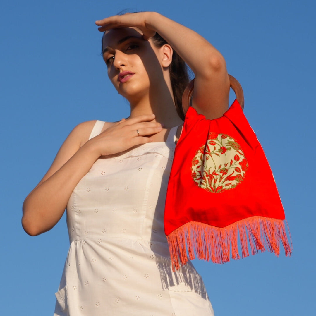 Woman holding a red scarf with gold design against a clear blue sky