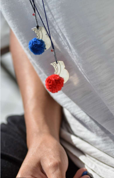 Necklace with blue and red pom-poms and a white crescent moon pendant on a blurred background.
