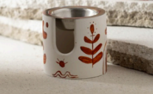 Ceramic candle holder with leaf patterns on a stone surface