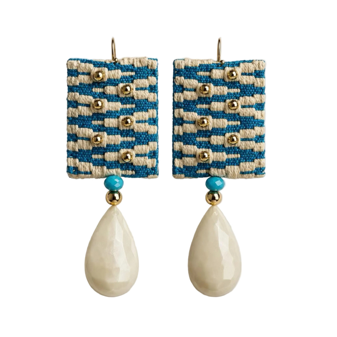 A pair of bohemian-style drop earrings featuring rectangular woven blue and cream fabric panels with gold-tone studs, a small turquoise bead, and a large cream teardrop bead dangling below.