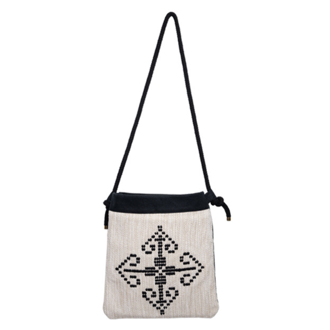 A handwoven cotton shoulder bag with a geometric pattern, predominantly white with black accents, and a black strap.
