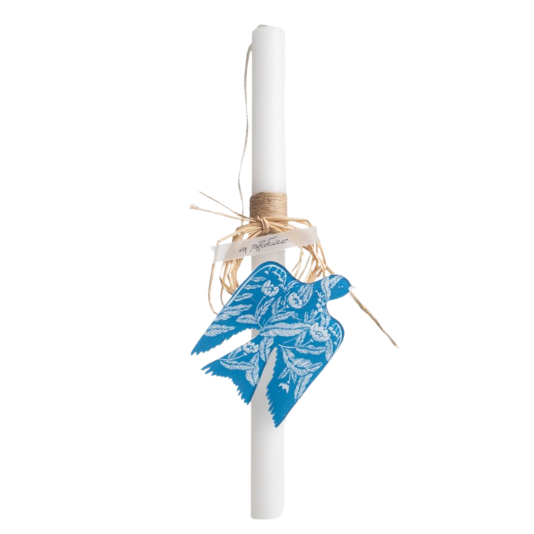 A white Easter candle with a minimalist bird design, adorned with a blue paper wing and placed against a white background.