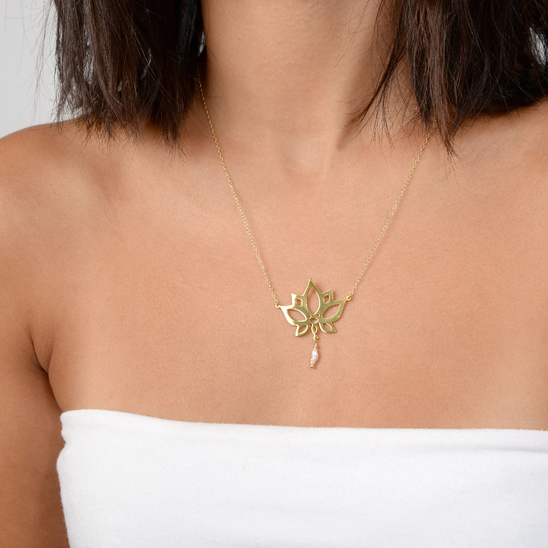 Gold necklace with a floral pendant on a person wearing a white top.