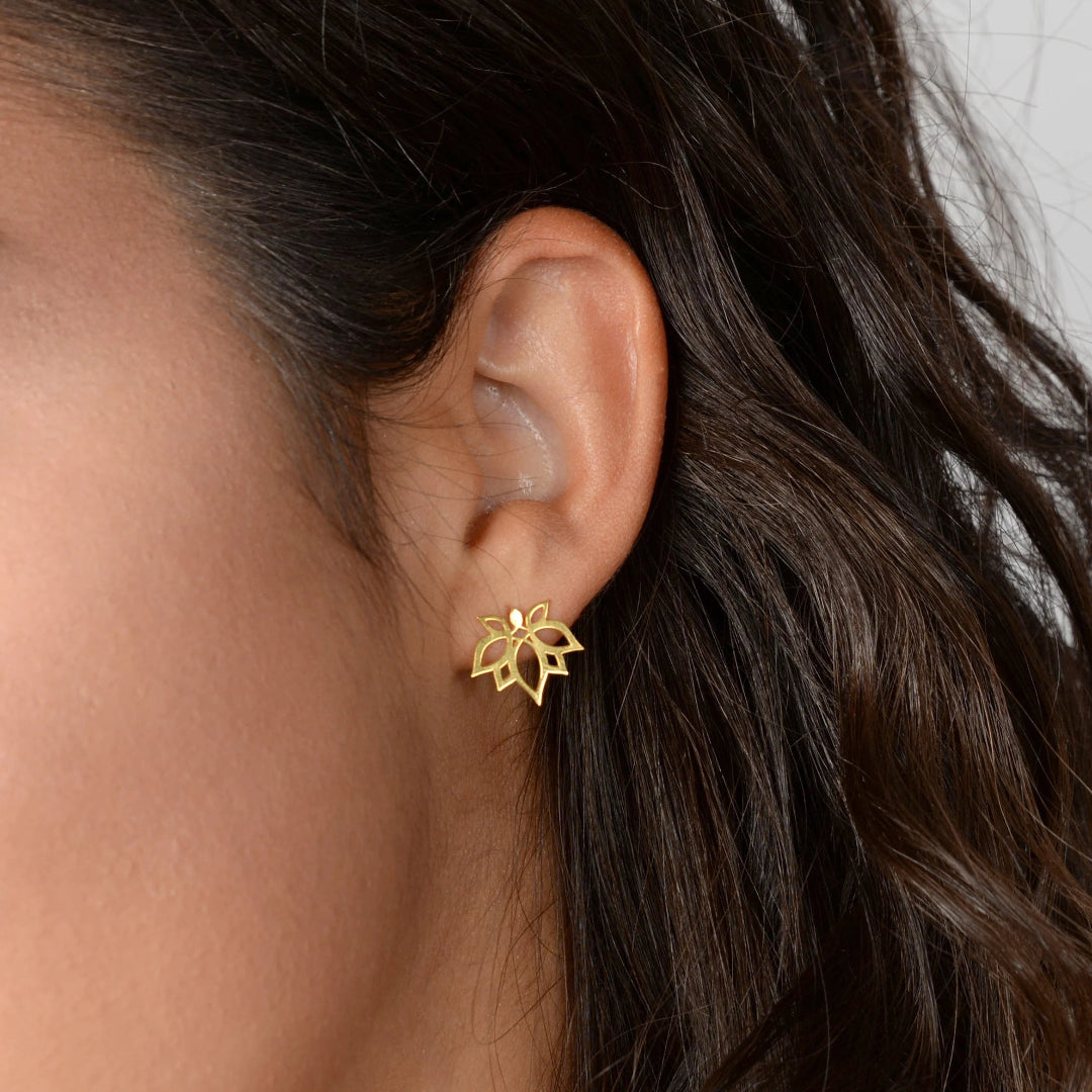 Gold lotus flower earring worn by a person with dark hair.