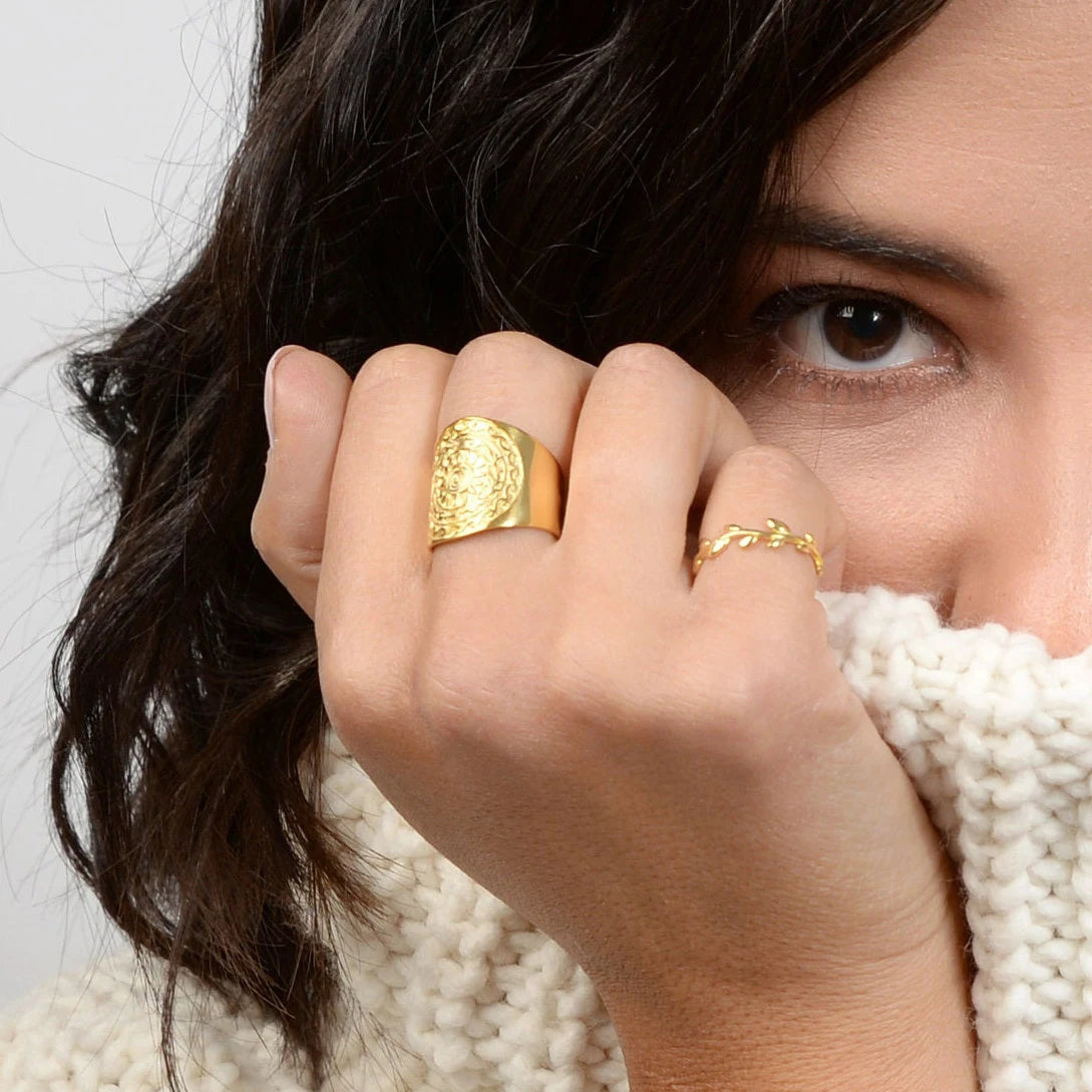 Close-up of a person wearing gold rings on a neutral background