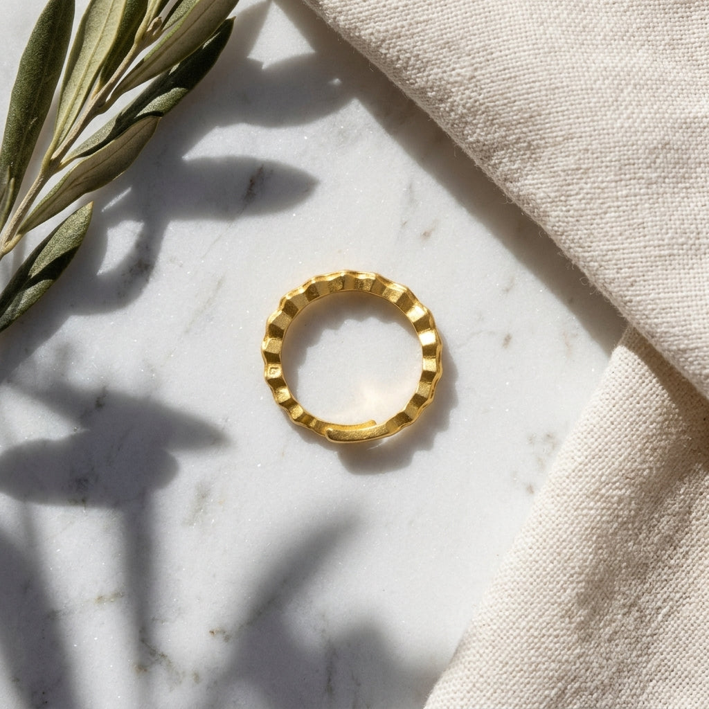 Gold ring on a marble surface with a beige fabric and olive branch