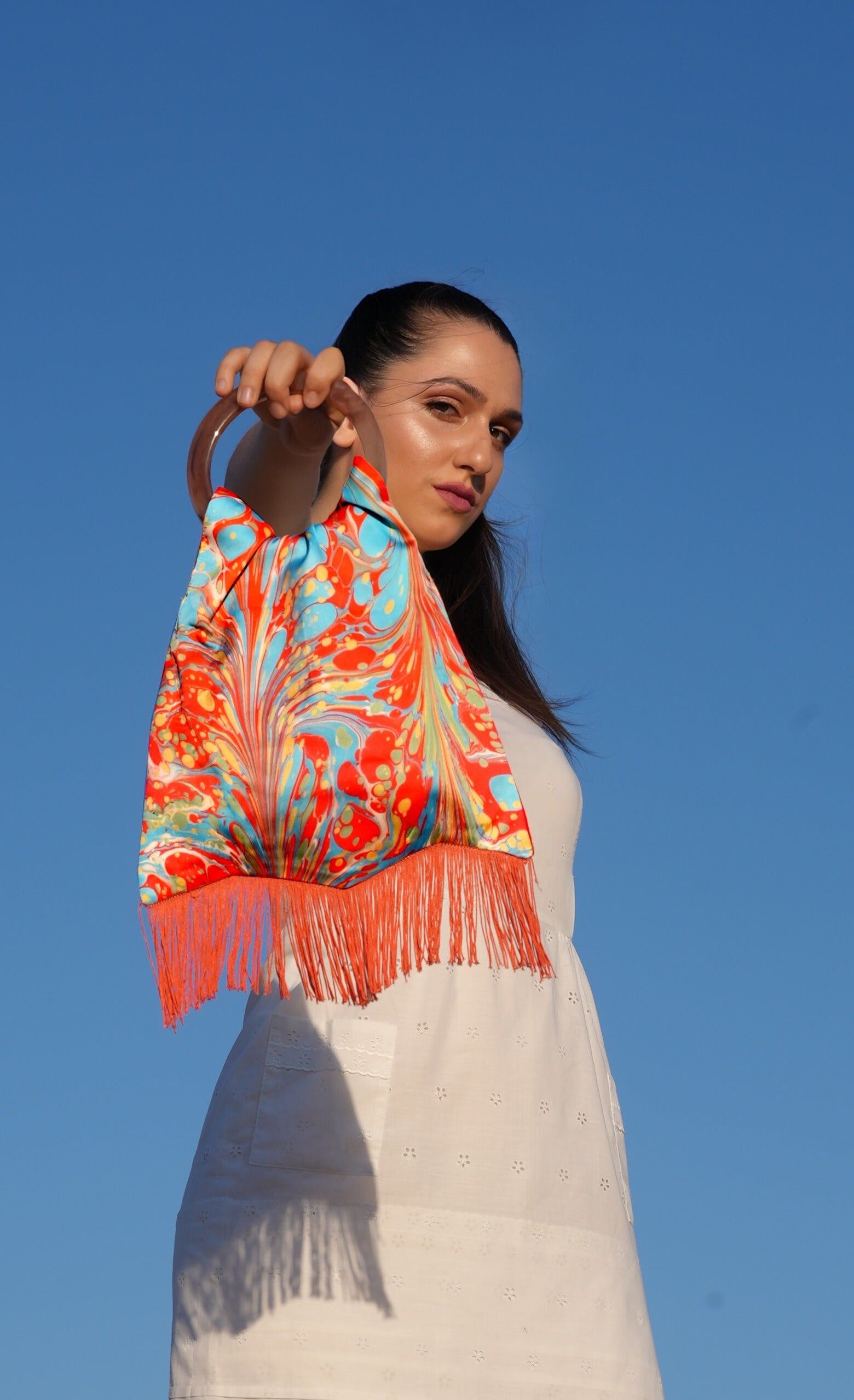 Woman holding a colorful scarf against a clear blue sky