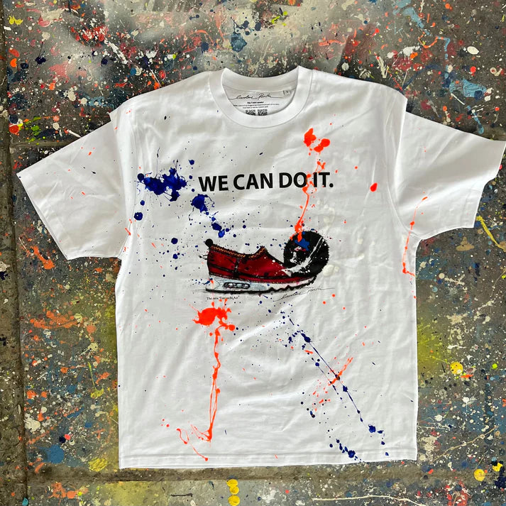 White t-shirt with 'WE CAN DO IT.' graphic on a textured surface with paint splashes
