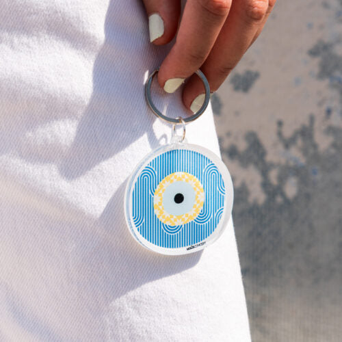 Round keychain with blue and white pattern held by a hand against a blurred background