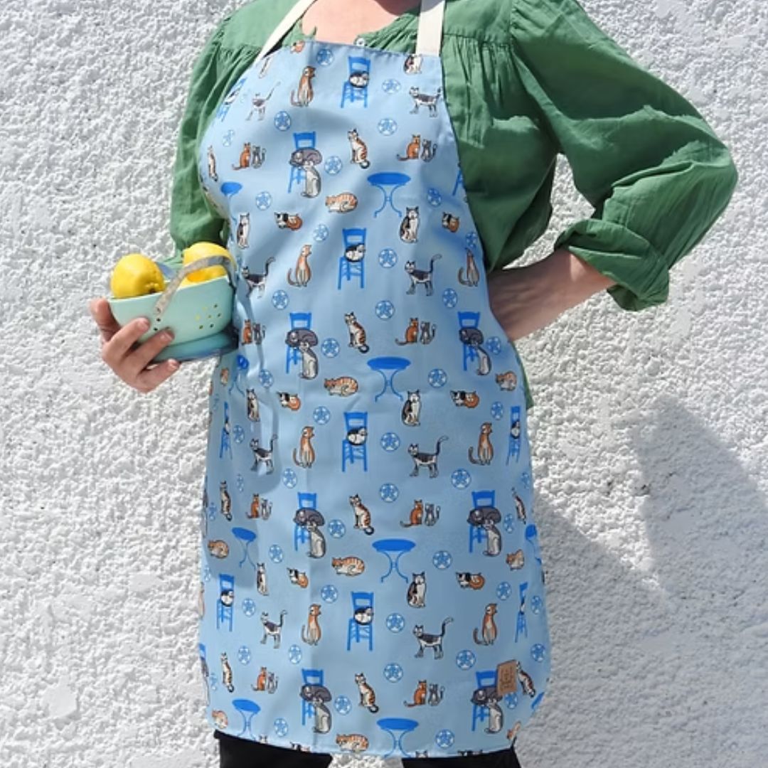 Greek Island Cats Apron – water-resistant apron with Greek cats, blue chairs and café tables on soft blue, worn, styled | Thalassea