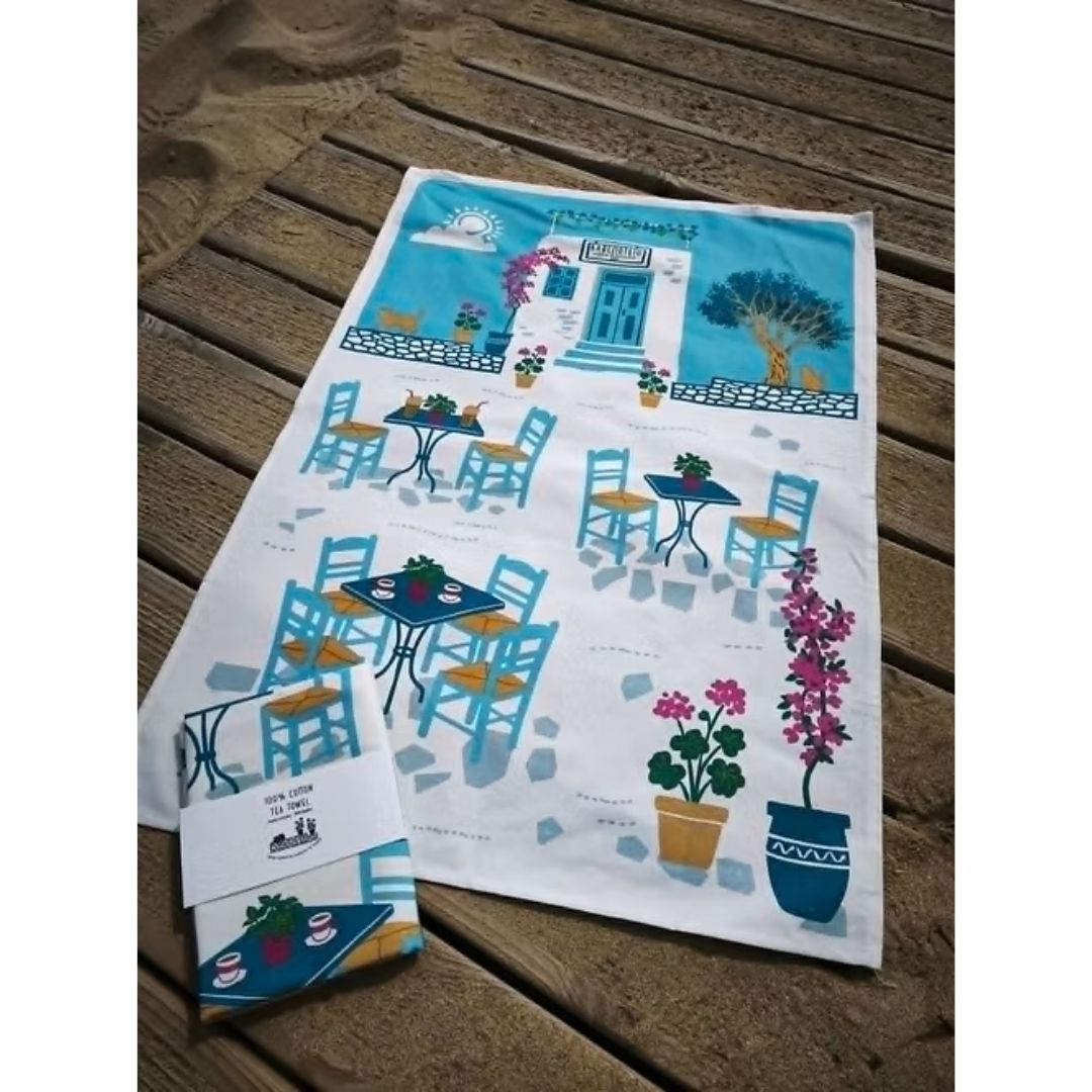 Coffee and Drinks Cotton Tea Towel – Greek kafeneio print laid flat on a timber deck beside a card-wrapped towel, styled | Thalassea