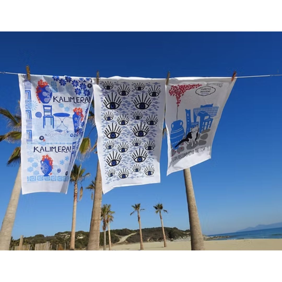 A Hue of Greek Blue cotton tea towels hanging by the sea, including the Blue Eye design, styled | Thalassea