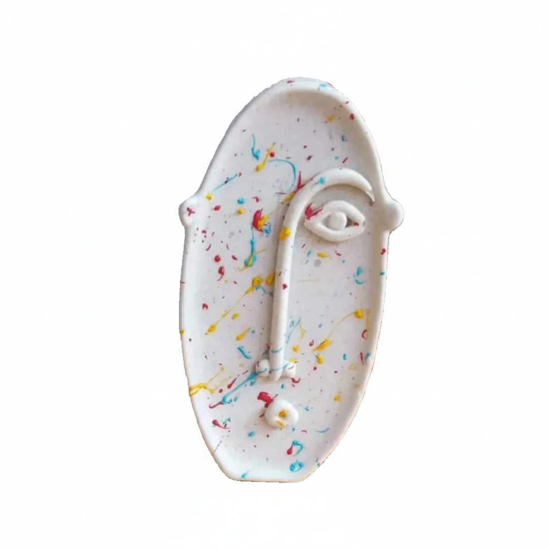 A ceramic face-shaped plate with colorful speckles on a white background