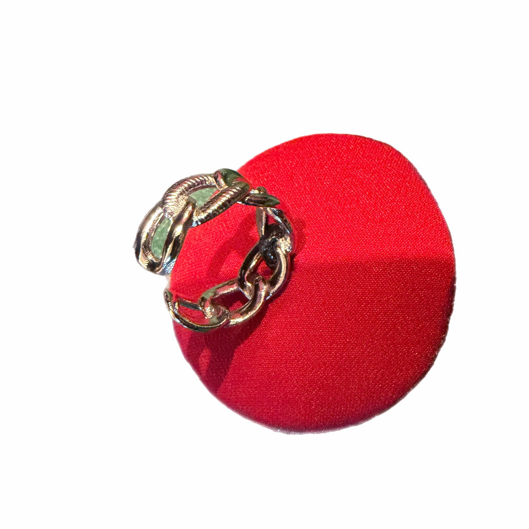 Gold ring with green gemstone on a red cushion against a white background