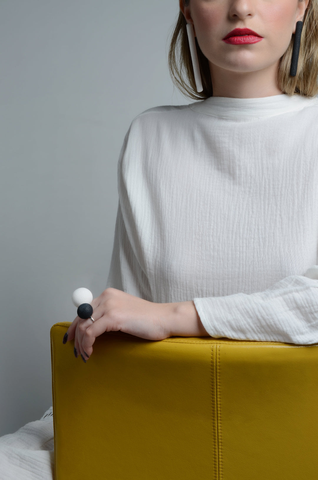 Woman in a white sweater sitting on a yellow chair against a gray background